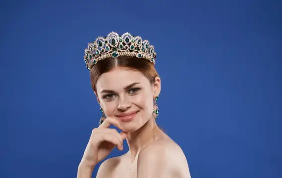 Молодая женщина в короне с изумрудами на синем фоне