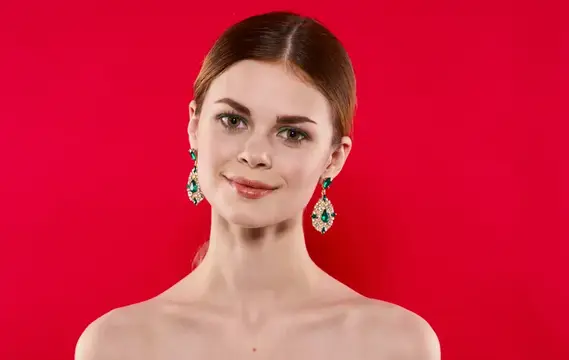 Привлекательная женщина с обнаженными плечами, украшениями и макияжем на роскошном красном фоне