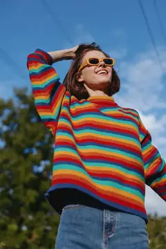 Улыбающаяся девушка в радужном свитере и желтых очках на фоне неба