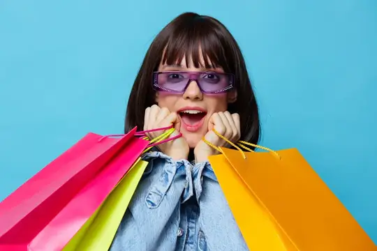 Восторженная девушка в фиолетовых очках с разноцветными пакетами