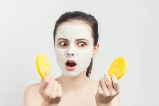 Удивлённая девушка с белой маской на лице и жёлтыми спонжами