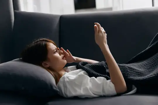 Молодая азиатская женщина лежит на диване и смотрит в смартфон