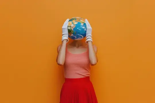 Женщина в белых перчатках держит глобус перед лицом на оранжевом фоне