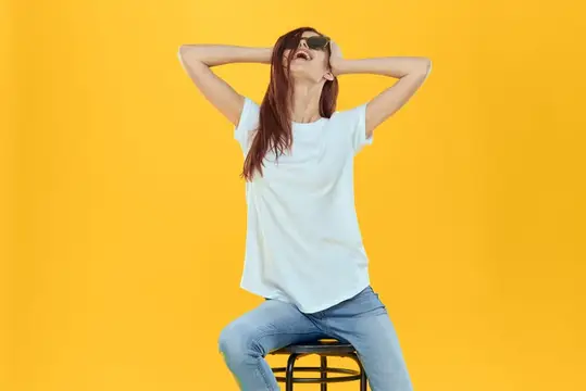 Девушка в солнцезащитных очках отдыхает на стуле на жёлтом фоне