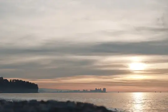 Закат над морем с силуэтом города на горизонте