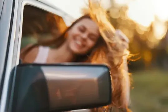 Улыбающаяся девушка с распущенными волосами выглядывает из окна автомобиля