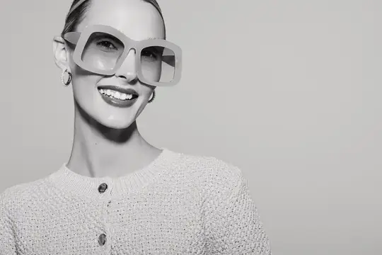 Счастливая светлокожая женщина европейской внешности в oversized-солнцезащитных очках и вязаном топе