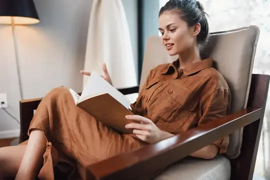 Молодая женщина с удовольствием читает книгу в уютном кресле