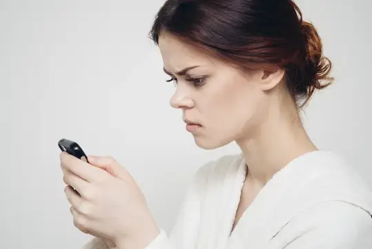 Молодая женщина с недовольным лицом смотрит в смартфон