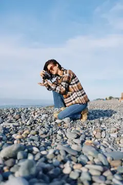 Девушка в клетчатой рубашке фотографирует на каменистом пляже