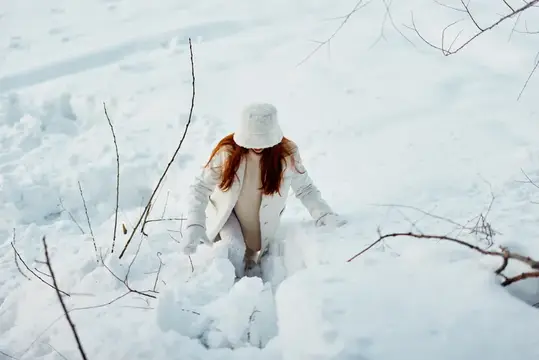 Молодая женщина улыбается, прогуливаясь в белом пальто, наслаждаясь зимним настроением и свежим воздухом