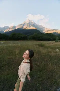 Молодая женщина с закрытыми глазами на лугу на фоне гор