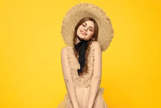 Улыбающаяся девушка в соломенной шляпе на жёлтом фоне