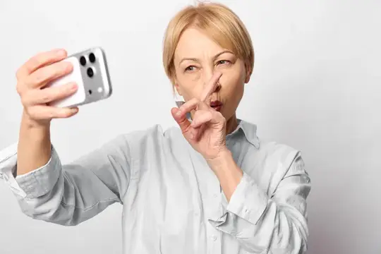 Удивлённая зрелая женщина держит смартфон для селфи