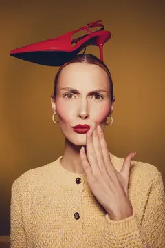 Женщина с красной туфлей на голове на жёлтом фоне