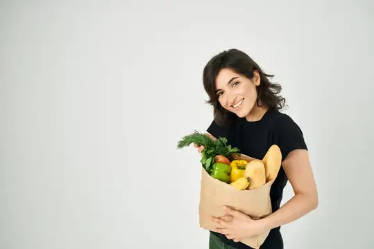 Весёлая брюнетка в чёрной футболке с пакетом продуктов из супермаркета, совершающая покупки