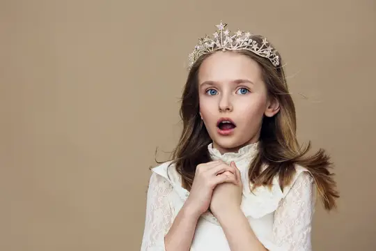 Удивлённая девочка в короне и белом платье на бежевом фоне