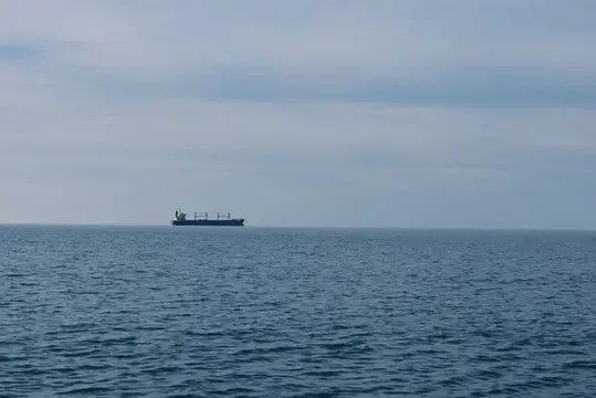 Грузовое судно плывёт по спокойному морю под пасмурным небом