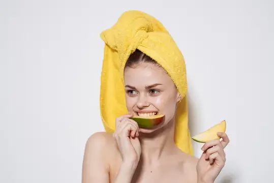 Улыбающаяся девушка с полотенцем на голове ест дыню