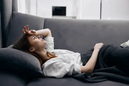 Уставшая молодая женщина лежит на диване, держась за голову