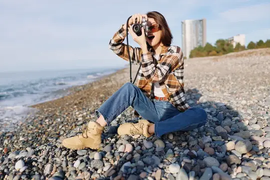 Молодая женщина фотографирует на пленочный фотоаппарат на галечном пляже