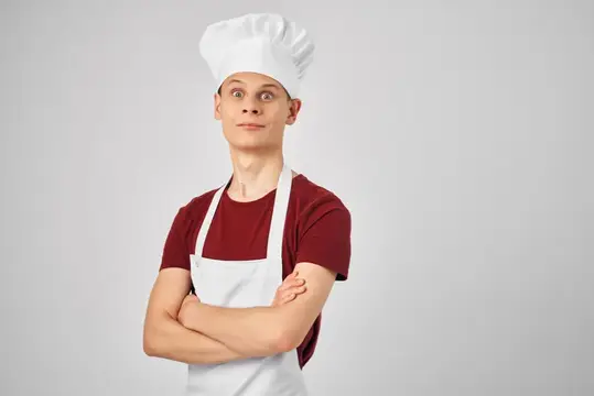 Молодой повар в колпаке и фартуке скрестил руки на груди