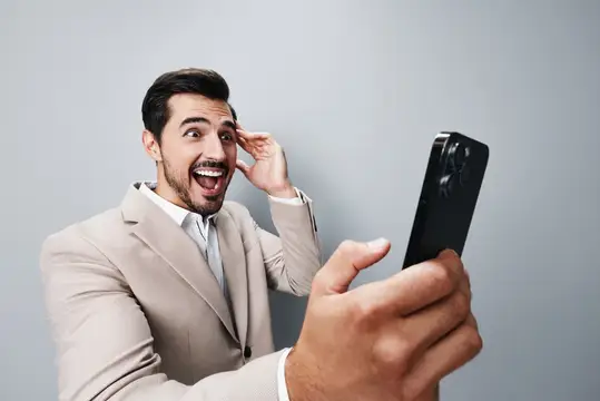 Деловой мужчина в костюме с улыбкой держит смартфон в студии на однотонном фоне