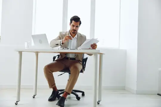 Уверенный мужчина держит документ и работает за ноутбуком