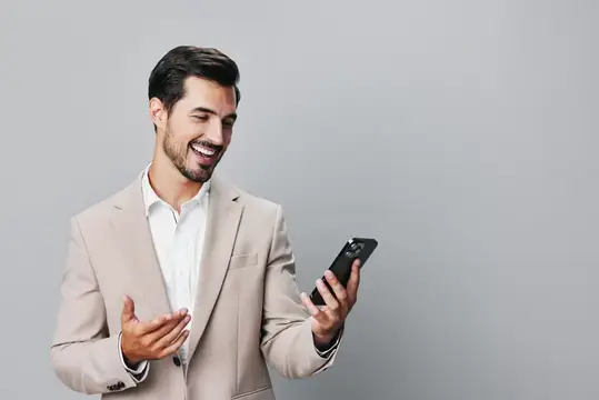 Улыбающийся мужчина в бежевом пиджаке смотрит на смартфон
