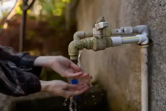 Руки набирают воду из уличного крана на бетонной стене