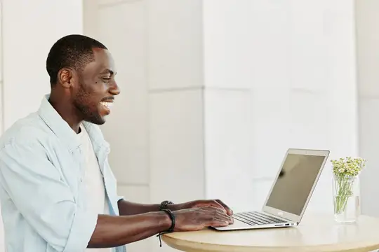 Улыбающийся темнокожий мужчина работает за ноутбуком в светлом офисе