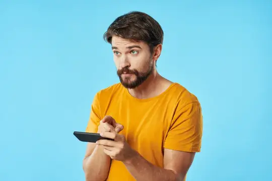 Мужчина в желтой футболке на синем фоне держит в руке мобильный телефон