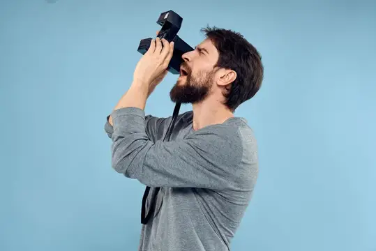 Бородатый мужчина пьёт из фотоаппарата на голубом фоне
