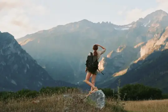 На сцене изображена одинокая туристка в футболке, шортах, походных ботинках и с рюкзаком