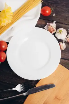 Белая тарелка с макаронами, помидорами и чесноком на тёмном столе