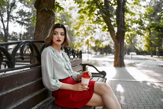Молодая женщина с кофе сидит на скамейке в парке