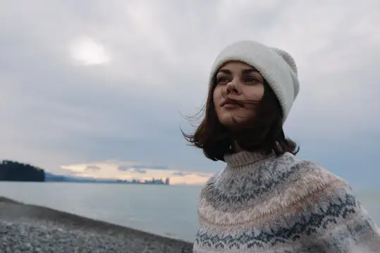 Молодая женщина в белой шапке на берегу моря в пасмурный день