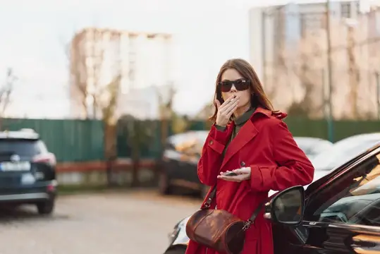 Яркая сцена: стильная женщина в красном пальто и солнцезащитных очках ест и улыбается