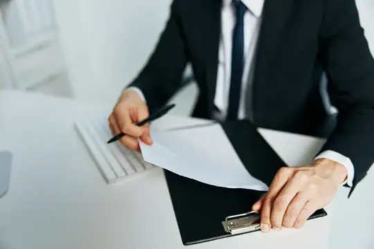 Мужчина в костюме подписывает документы за рабочим столом