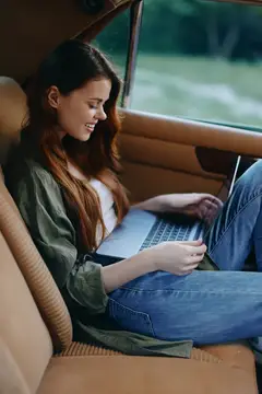 Улыбающаяся девушка с ноутбуком на заднем сиденье автомобиля