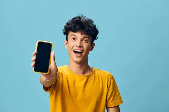 Кудрявый парень в жёлтой футболке показывает смартфон на голубом фоне