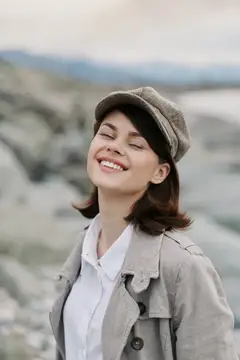 Улыбающаяся девушка в кепке и плаще на фоне гор