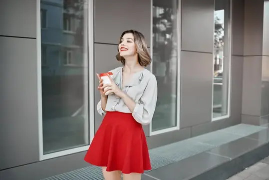 Улыбающаяся девушка в красной юбке с кофе у стеклянного фасада