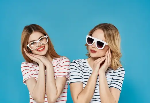 Две улыбающиеся девушки в солнцезащитных очках на голубом фоне