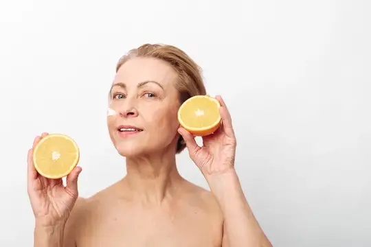 Зрелая женщина с дольками апельсина у лица на белом фоне