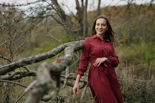 Улыбающаяся девушка в бордовом платье у поваленного дерева