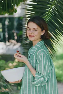 Улыбающаяся темноволосая девушка с ягодой и миской на фоне пальмы
