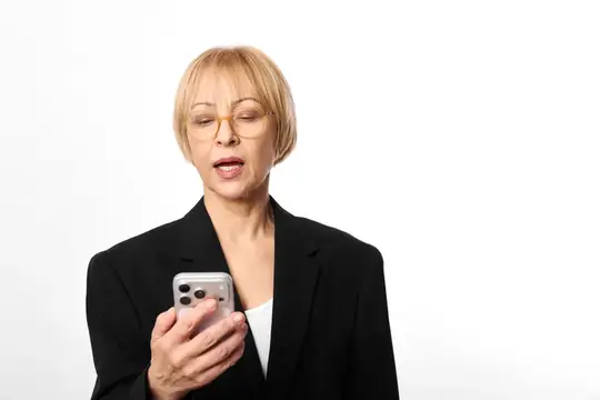 Блондинка в очках и чёрном пиджаке удивлённо смотрит в смартфон