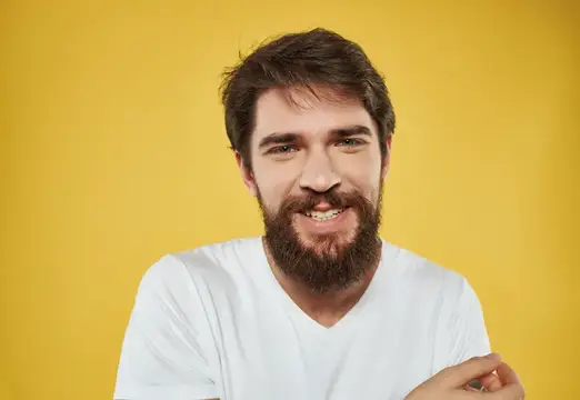 Улыбающийся бородатый мужчина в белой футболке на жёлтом фоне