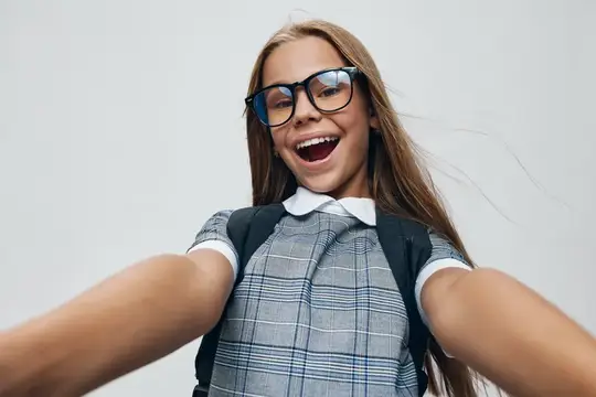 Смеющаяся школьница в очках делает селфи на светлом фоне